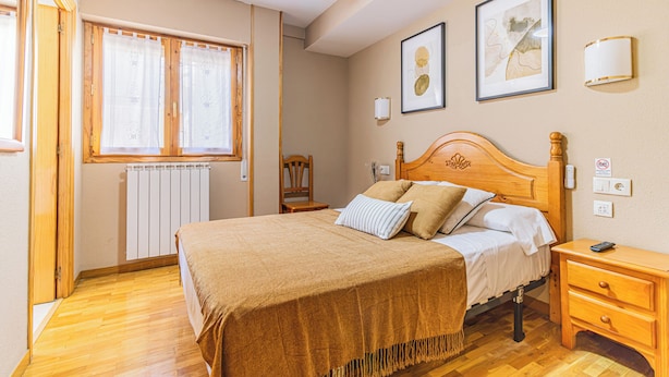Un dormitorio con una cama de madera, una mesita de noche, una silla, un radiador y dos cuadros en la pared.