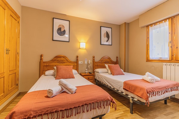 Habitación de hotel con dos camas, cabeceros de madera, una mesita de noche, una lámpara de pared y un ventanal con cortinas.