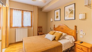 Um quarto com cama, mesa de cabeceira, cadeira, radiador e janela com cortinas.