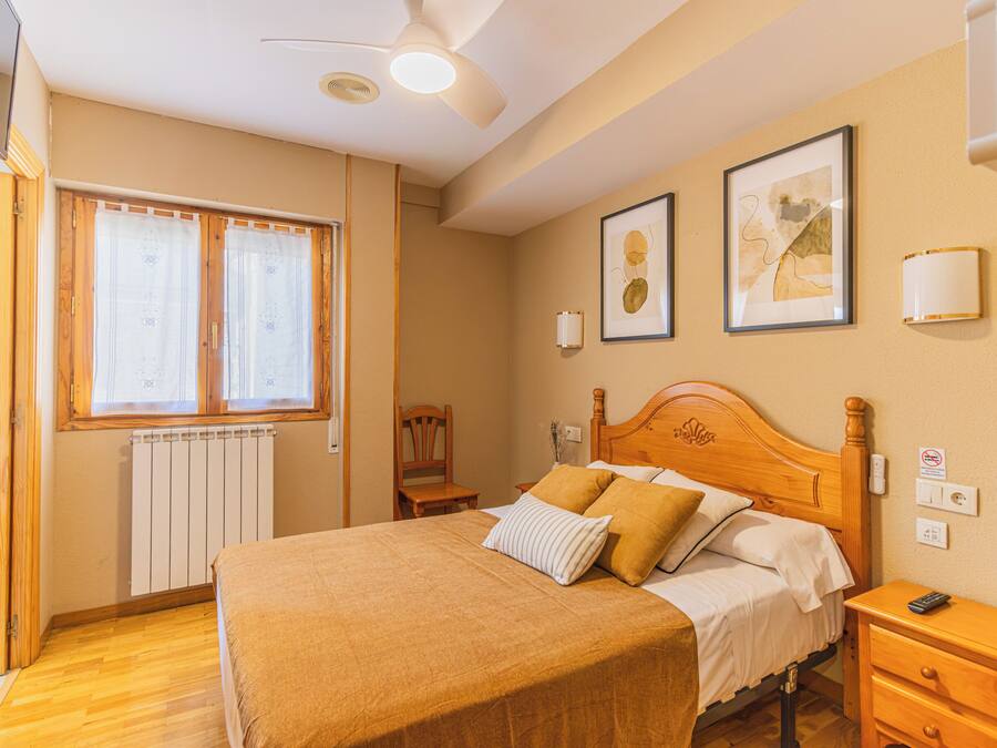 A bedroom with a bed, a nightstand, a chair, a radiator, and a window with curtains.