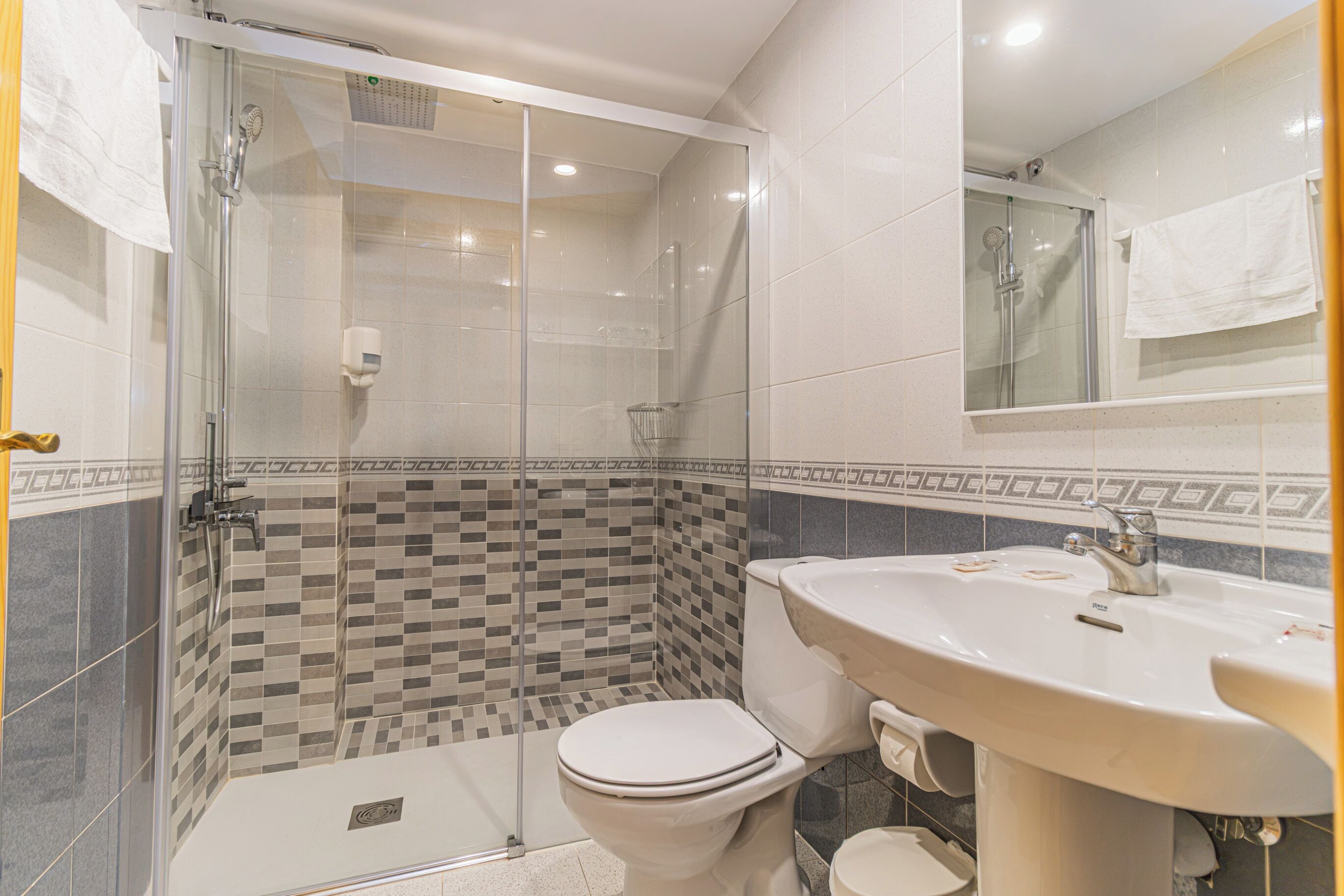 Un baño con ducha de vidrio, inodoro y lavamanos con espejo.