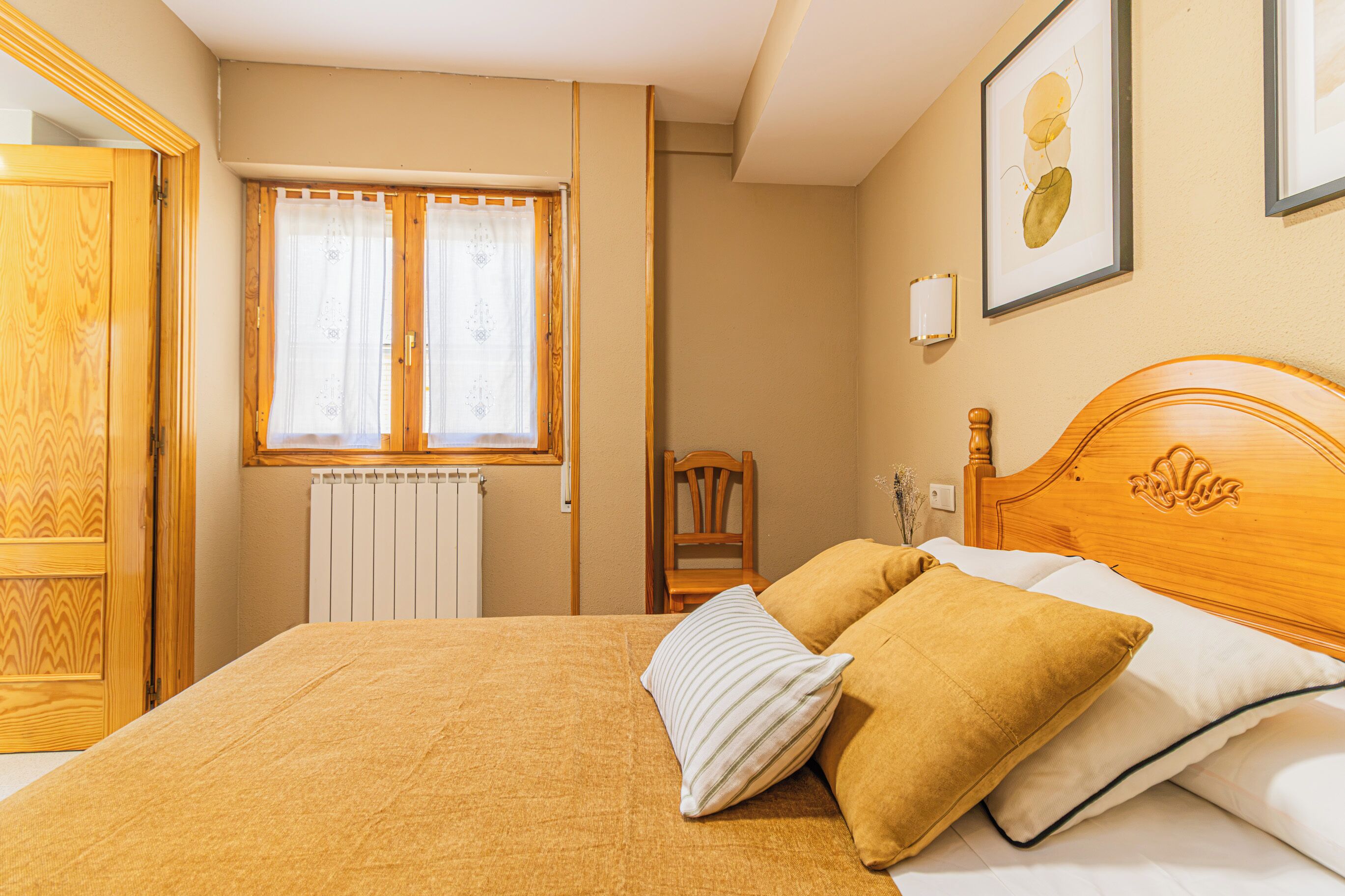 Ein Hotelzimmer mit Bett, einem Fenster mit Vorhängen, einem Heizkörper, einem Sessel und einer Wandleuchte.
