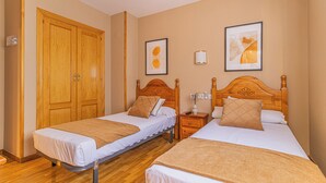 Quarto de hotel com duas camas de solteiro, cabeceiras de madeira, um guarda-roupa e dois quadros na parede.