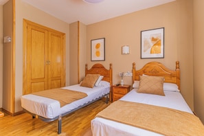 Habitación de hotel con dos camas individuales, cabeceros de madera, un armario y dos cuadros en la pared.