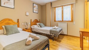 Habitación de hotel con dos camas, una ventana con cortinas, un radiador y suelo de madera.