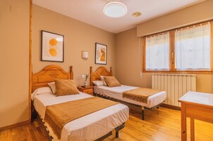 A hotel room with two beds, a wooden headboard, a bedside table, a nightstand, a window with a view, and a radiator.
