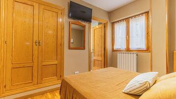 Een slaapkamer met een bed, een televisie, houten kasten, een raam met gordijnen en een radiator.