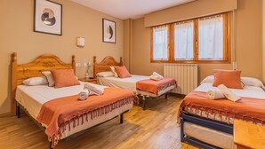 Habitación de hotel con tres camas, un ventilador de techo y una ventana con cortinas.