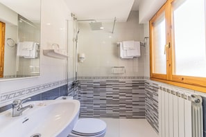 Un baño moderno con cabina de ducha de vidrio, un lavabo blanco y un inodoro.