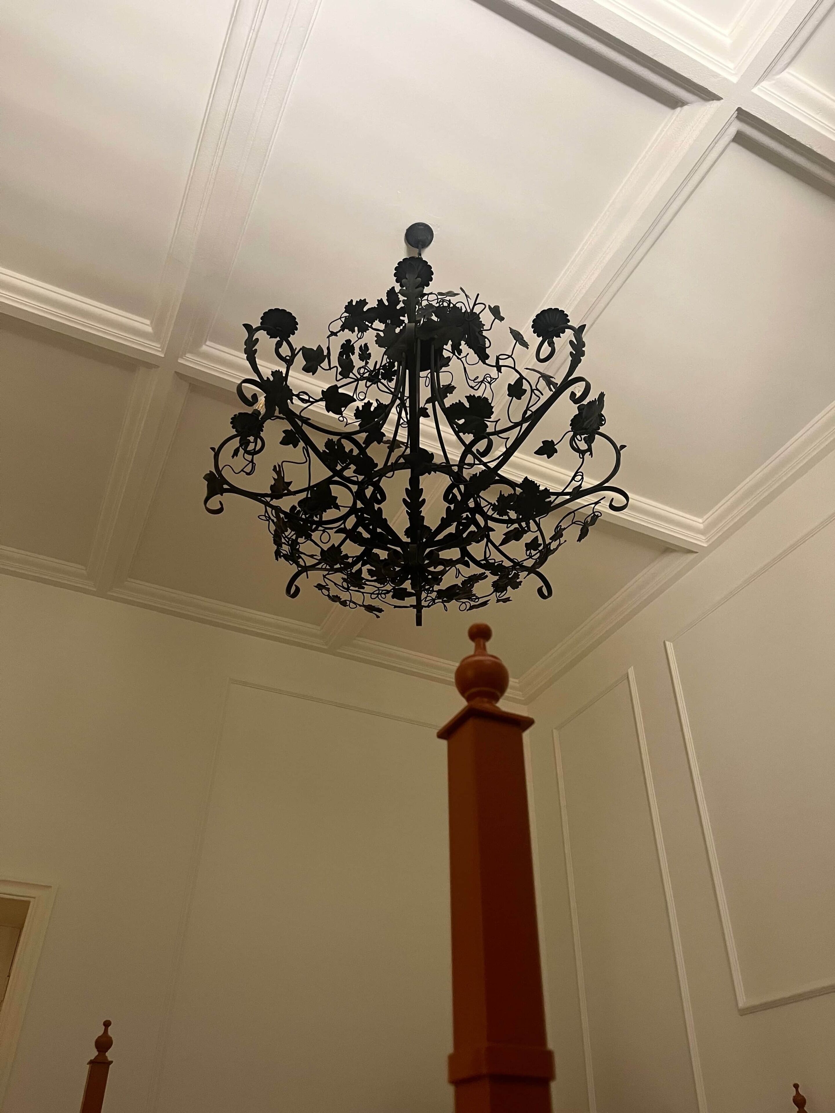 Quarto com teto e lustre decorativo, paredes brancas e um pilar de madeira.