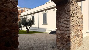 An outdoor courtyard with stone columns, a tree, and a building with white walls and shutters.