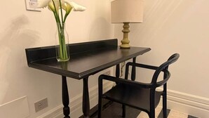 A small table with a vase of flowers, a lamp, and two chairs in a corner.