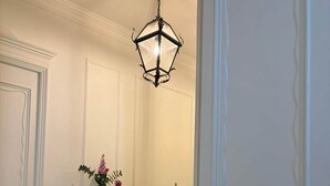A hallway with a checkered floor, a wooden cabinet, a vase with flowers, and a hanging light fixture.