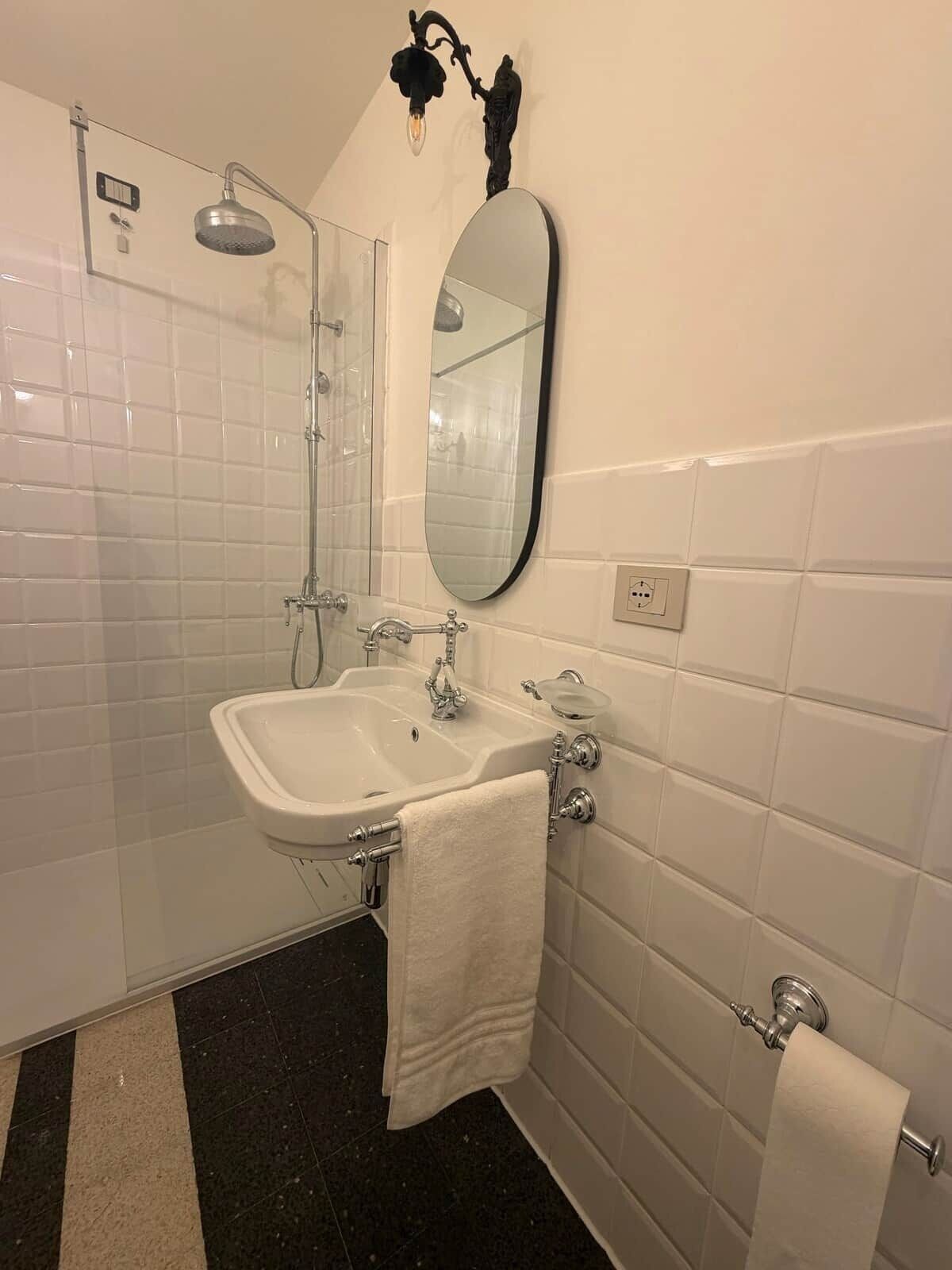 A bathroom with a white sink, a mirror, a towel rack, a shower, and a toilet.