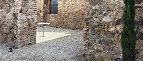 An ancient stone archway, a potted evergreen, and a gravel courtyard.