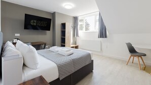 A modern hotel room with a bed, a desk, a chair, and a TV displaying 'GUEST READY'. - Comfortable King Room with Private Bathroom (Watford)