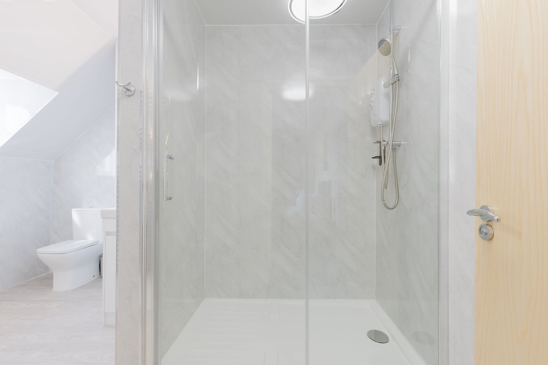Une salle de bain moderne avec une douche à parois de verre, des toilettes et une porte en bois.