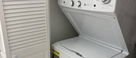 A front-loading washing machine with a control panel, a door with a handle, and a label on the door.