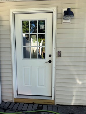 A white front door with a glass panel, a black doorbell, and a wall-mounted light fixture.