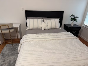 A bedroom with a bed, bedside table, chair, and a potted plant.