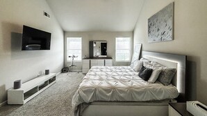 Une chambre avec un lit, un téléviseur fixé au mur, un bureau et une fenêtre.