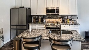 Une cuisine avec des armoires blanches, un réfrigérateur en acier inoxydable, un four à micro-ondes, une cuisinière et deux tabourets de bar.