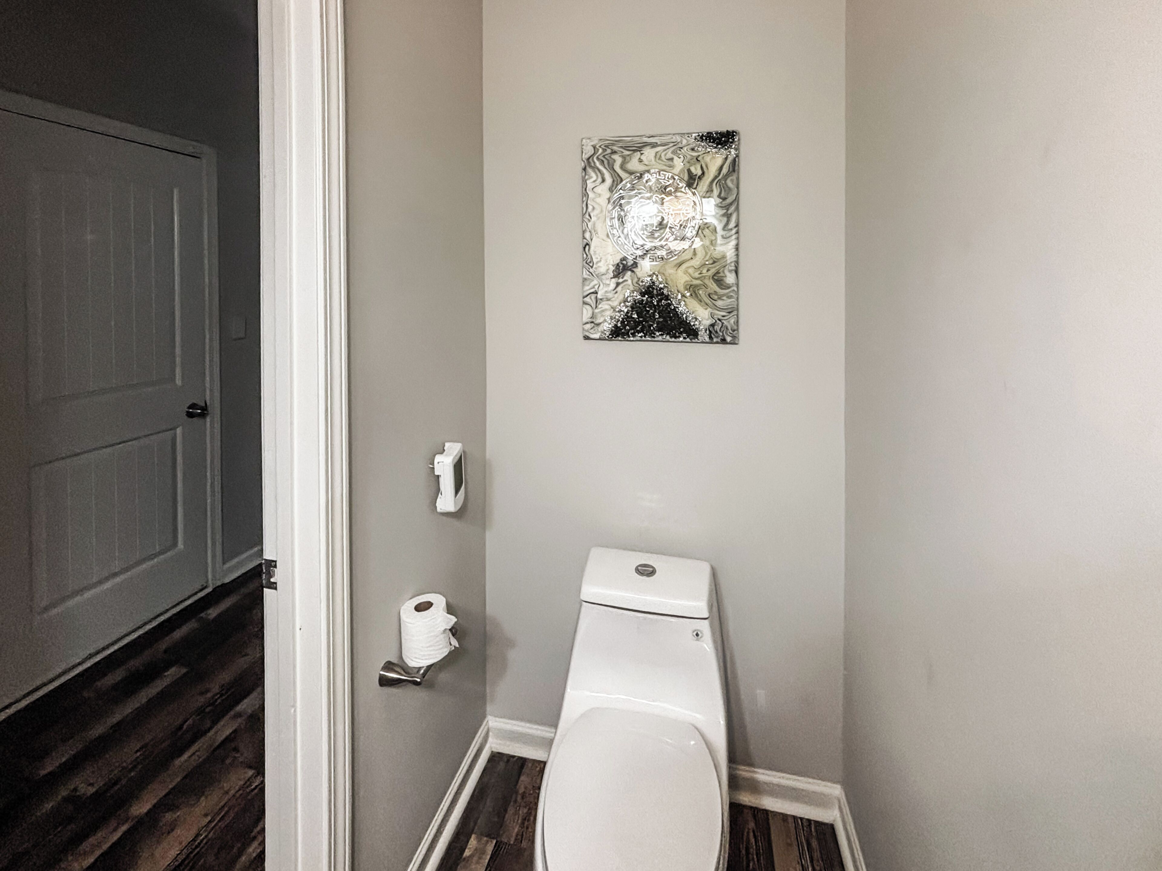 A bathroom with a toilet, a roll of toilet paper, and a wall-mounted abstract art piece.