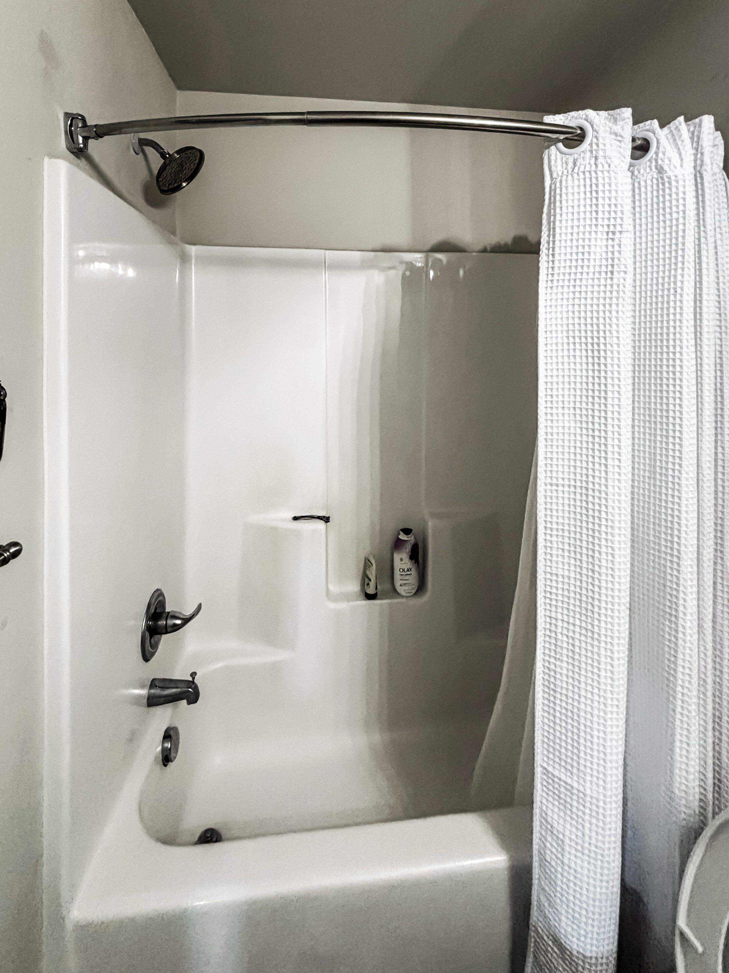 A white bathtub with a shower curtain, a handheld showerhead, and a bottle of Olay shampoo.