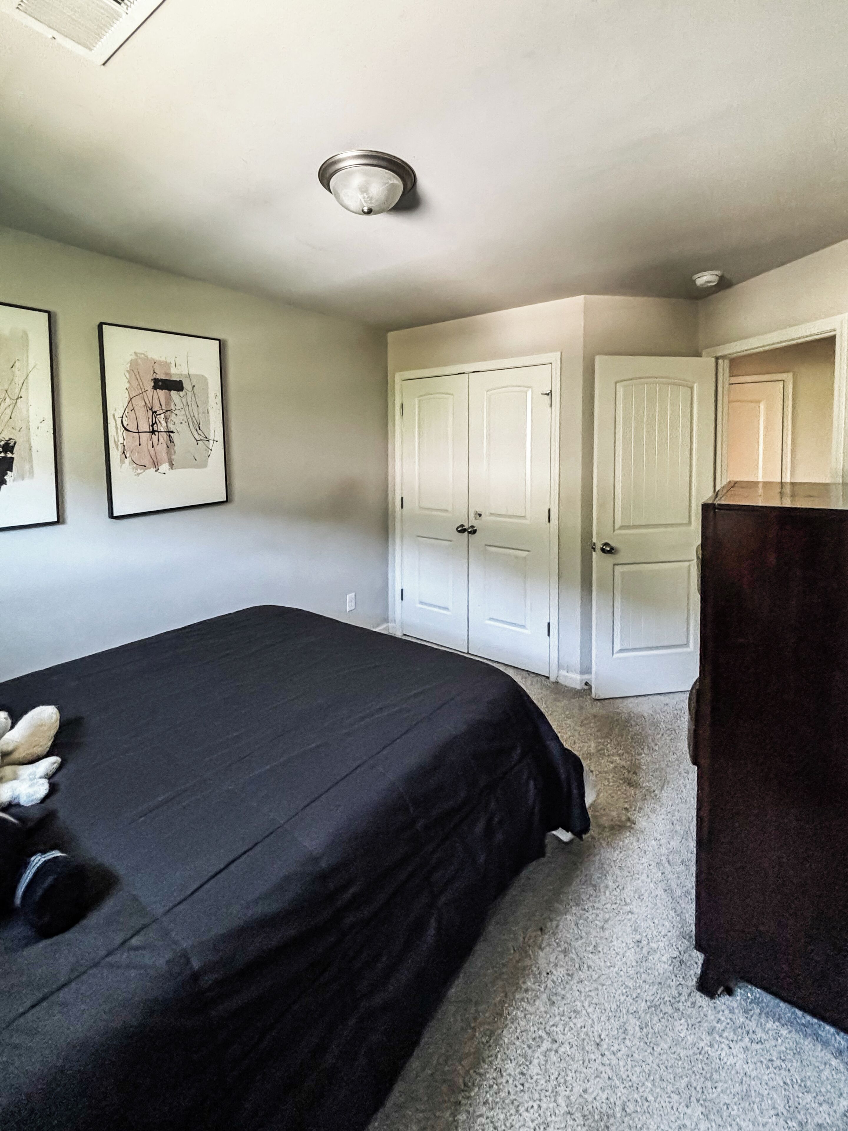 Un dormitorio con una cama, dos puertas, un aparador y dos cuadros en la pared.