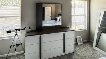 Une chambre à coucher comprenant un lit, une commode, un télescope et deux fenêtres équipées de stores.