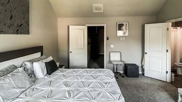 Un dormitorio con una cama grande, un ventilador de techo, una puerta que da a otra habitación y una mesita con una silla.
