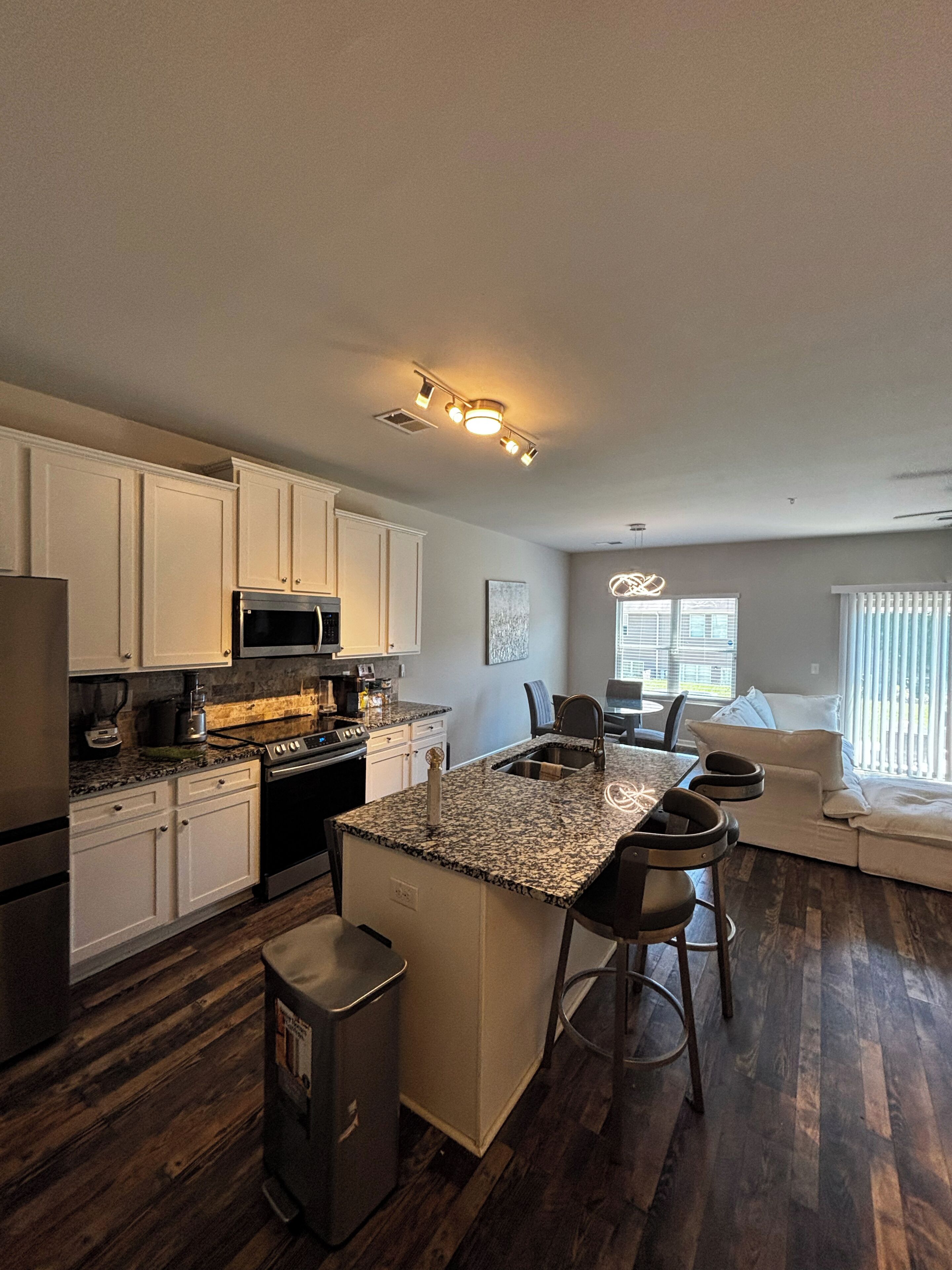 A modern kitchen with white cabinets, a granite countertop, stainless steel appliances, and a central island with bar stools.