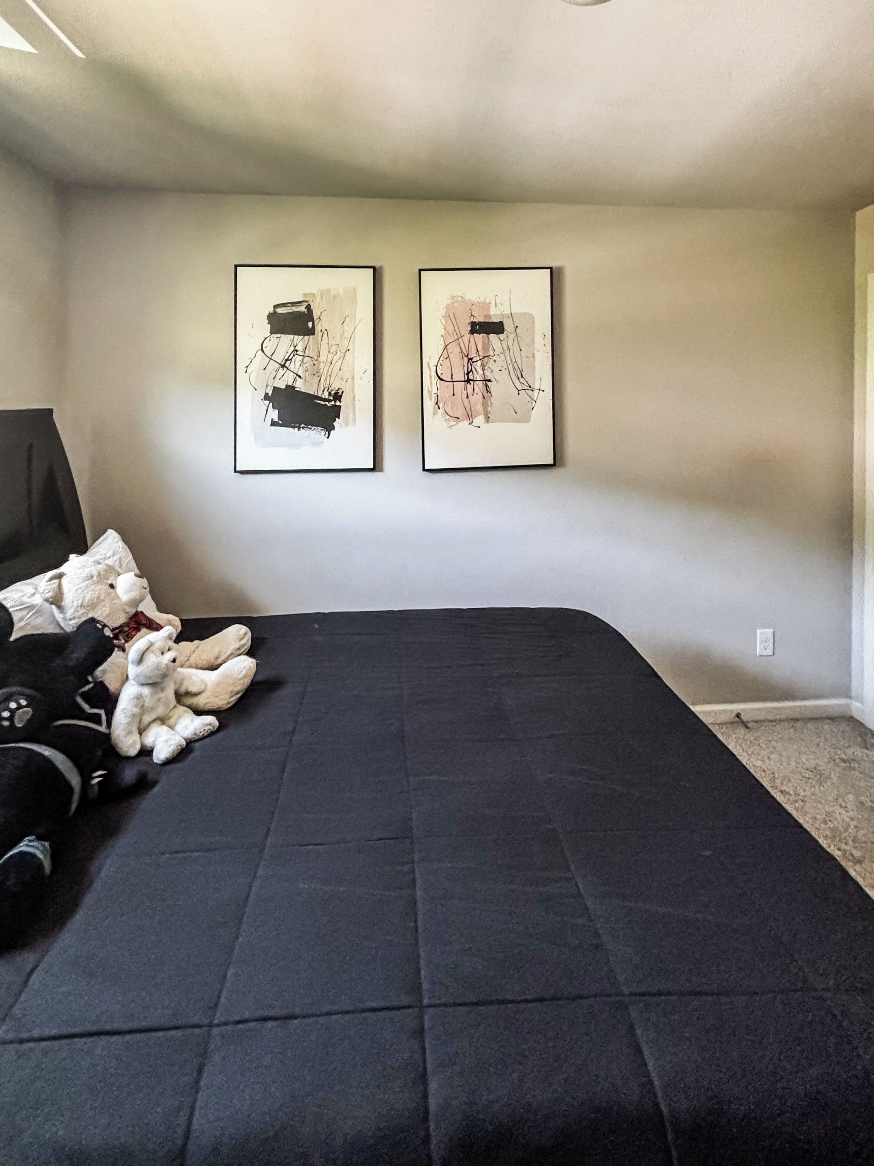 Slaapkamer met een zwart beddekleed, twee ingelijste abstracte schilderijen aan de muur en een teddybeer op het bed.