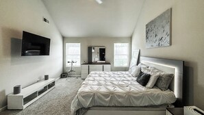 Une chambre à coucher comprenant un lit, un bureau, une chaise, un téléviseur et un ventilateur de plafond.