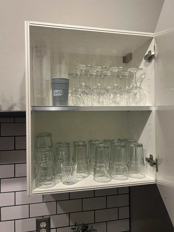 A cabinet with two shelves containing wine glasses and a tumbler.