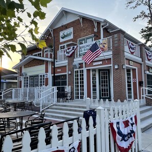 A restaurant with outdoor seating, a white picket fence, and American flags.