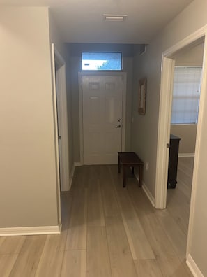 A hallway with a white door, a small table, and a window with blinds.