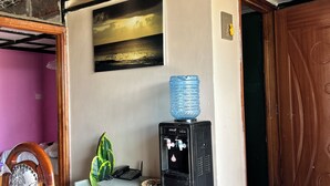 Una habitación con dispensador de agua, un cuadro, una planta en maceta y una puerta de madera.