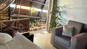 Una habitación con una cama, un sillón gris, un sillón colgante y un pequeño jardín con plantas.