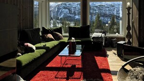 Ein gemütliches Zimmer mit einem grünen Sofa, einem roten Teppich und Blick auf schneebedeckte Berge durch große Fenster.
