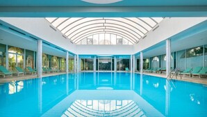 Una piscina interior con techo de vidrio, sillones de descanso y vistas al cielo.