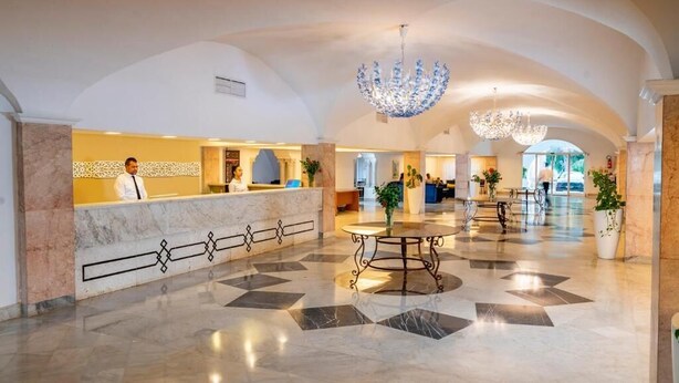 Un vestíbulo de hotel con piso de mármol, un mostrador de recepción y un candelabro.