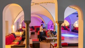 Un amplio salón con asientos rojos y negros, una mesa central y una cabina de DJ.
