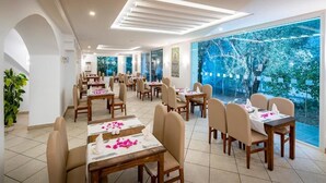 Comedor con varias mesas y sillas, ventanas amplias con vistas a zonas verdes y un diseño de techo moderno.