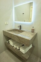 Un baño con un lavamanos grande y rectangular, un espejo encima y un estante abajo con toallas dobladas.
