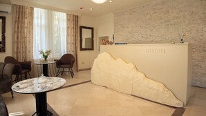 Un taulell de recepció de disseny únic, una zona d'estar amb dues cadires i una taula, i un mirall gran a la paret.