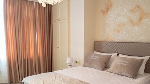 Una habitació d'hotel amb un llit gran, un capçal de llit, una làmpada de paret, una finestra amb cortines i un sòl amb moqueta.