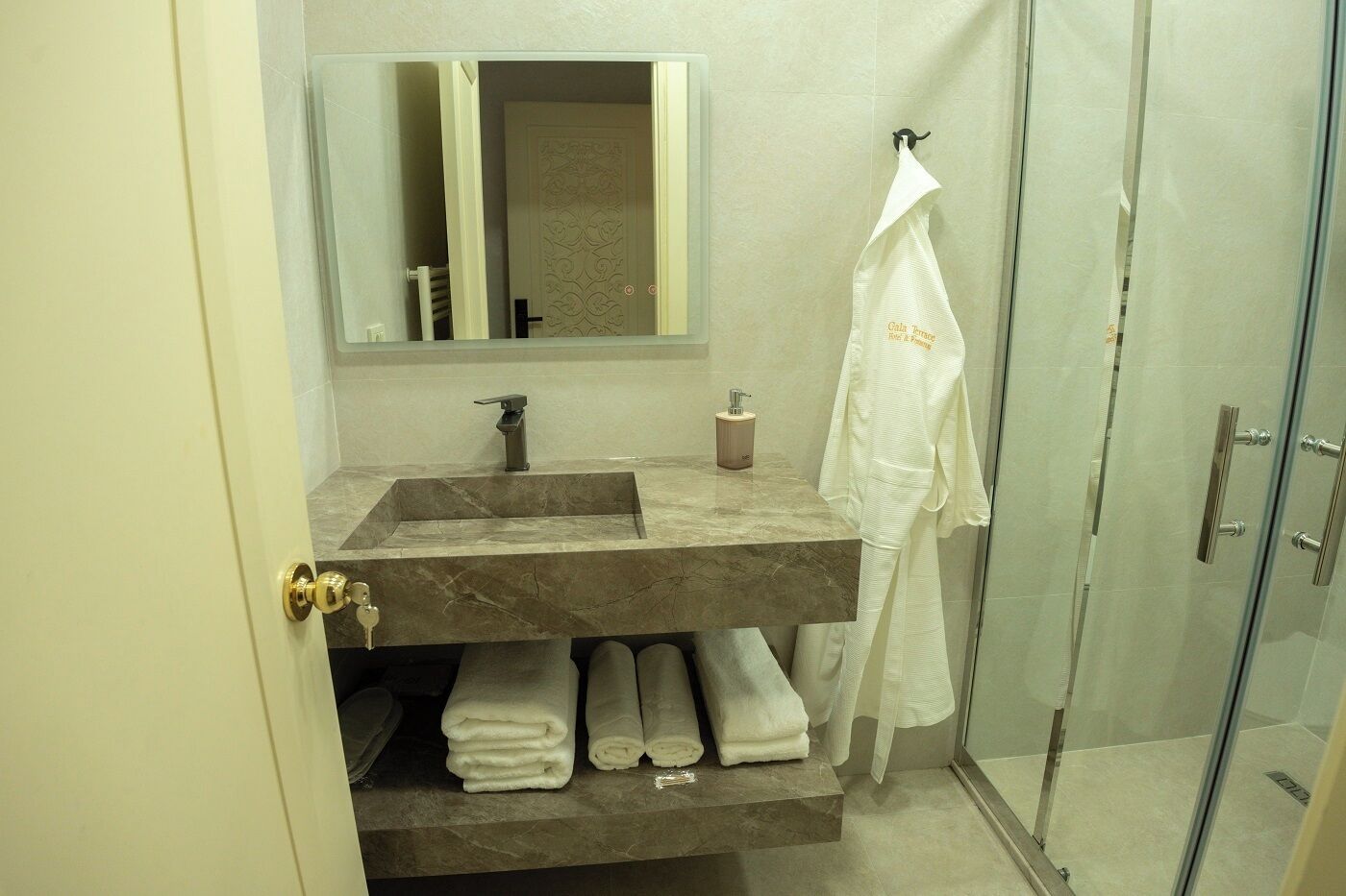 Un baño con lavamanos de mármol, un espejo, toallero con una toalla blanca y puerta de vidrio para la ducha.
