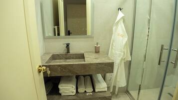 Un baño con lavamanos de mármol, un espejo, toallero con una toalla blanca y puerta de vidrio para la ducha.