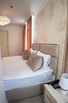 Een net opgemaakt bed met kussens, een nachtkastje met een lamp en een telefoon.